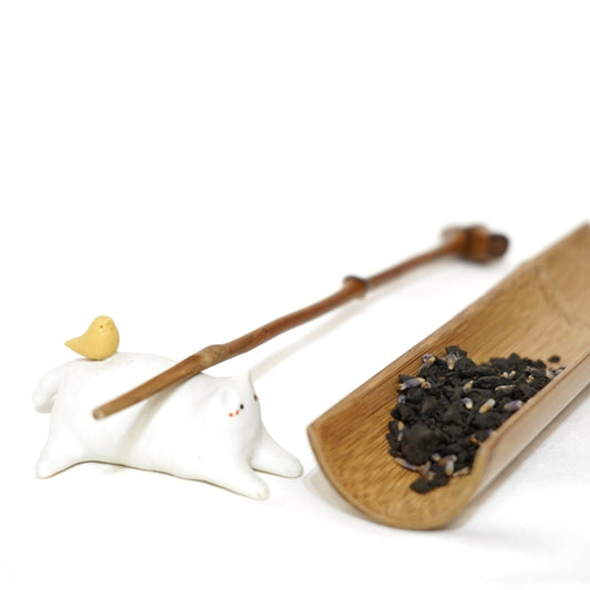 award winning lavender puerh tea  presented on a wooden tray, including a small amount of loose tea and a teapot spoon, with a white background.